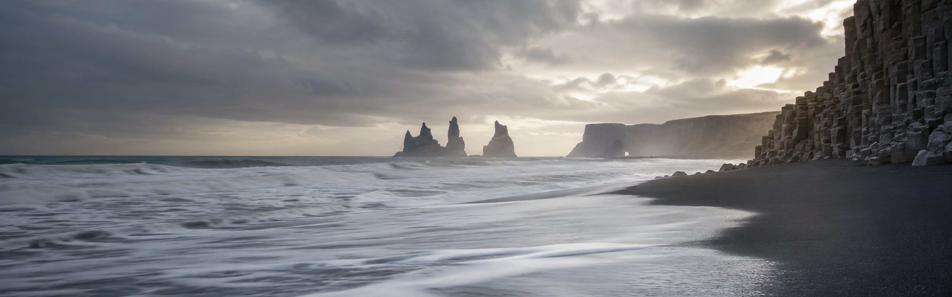 Icelandic black sand beach with basalt cliffs and distant sea stacks